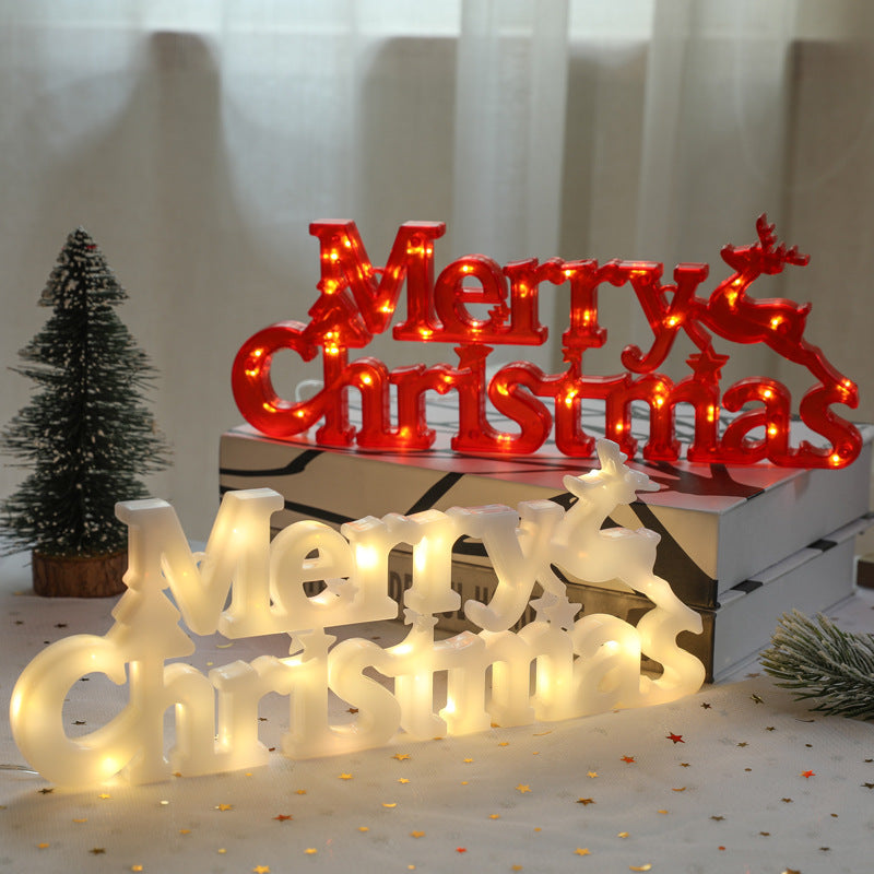 Decorative LED signs spelling 'Merry Christmas' on a table with a white curtain background.